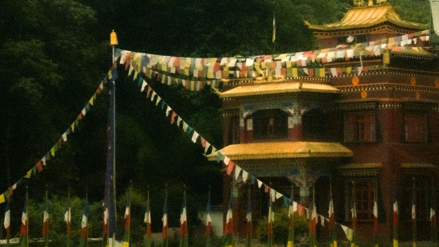 A monastery behind rows of prayer flags under a heavy sky
